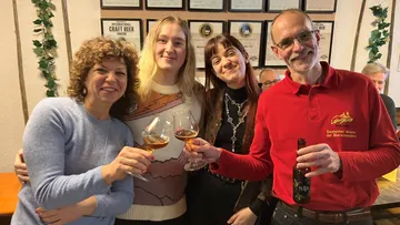 Four people smiling and toasting with drinks, indoor setting.