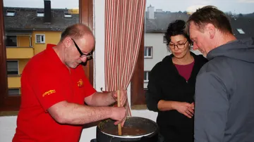 Man stirring pot while two others watch.