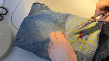 Person cutting denim with scissors, sun embroidery.