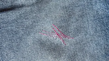 Blauer Jeansstoff mit rotem, genähtem Patch.