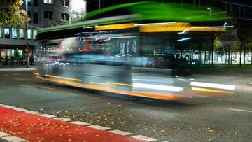 Blurred bus speeds through city intersection at night.