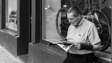 Man reading magazine outside bicycle shop.