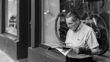 Man reads newspaper outside bike shop.