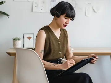 Junge Frau zeichnet konzentriert auf einem Tablet in einem Raum.