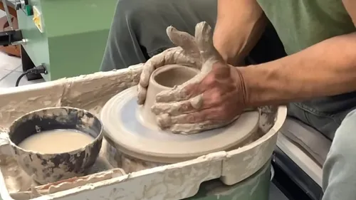 Person, die Ton auf einer Töpferscheibe formt.