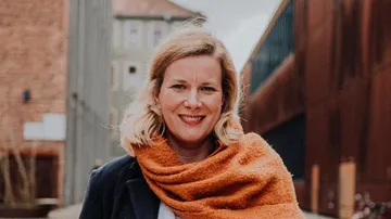 Person, die draußen lächelt, mit orangefarbenem Schal.