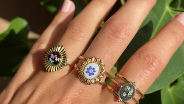 Three floral rings on a hand with nails.