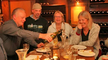 Mann gießt Wein für drei Freunde an einem Tisch ein.