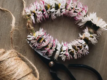 Wreath of flowers is placed on a wooden surface, with scissors and string.