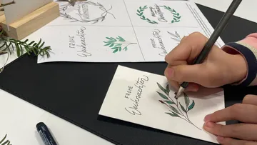 Person writing on card with plant design.