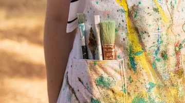 Pinsel in der Tasche mit bespritzter Schürze.