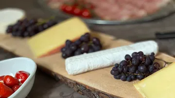 Cheese, grapes, and wrapped food on board.
