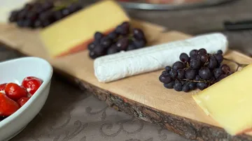 Käse, Trauben und geröstete Paprika auf einem Holzbrett.