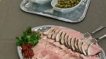 Sliced ham and tomatoes with olives on trays.