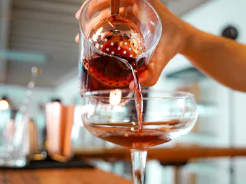 A glass is filled with red drink, bar environment.