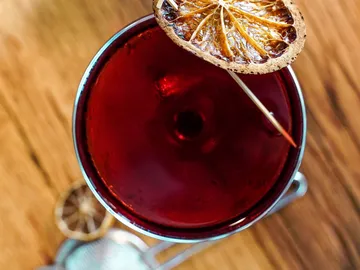 A red drink with burnt lemon stands on wood.