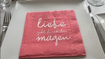 Rosa Serviette mit Text auf weißem Teller.