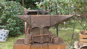 Rustikaler Amboss auf einem Holzblock im Freien.
