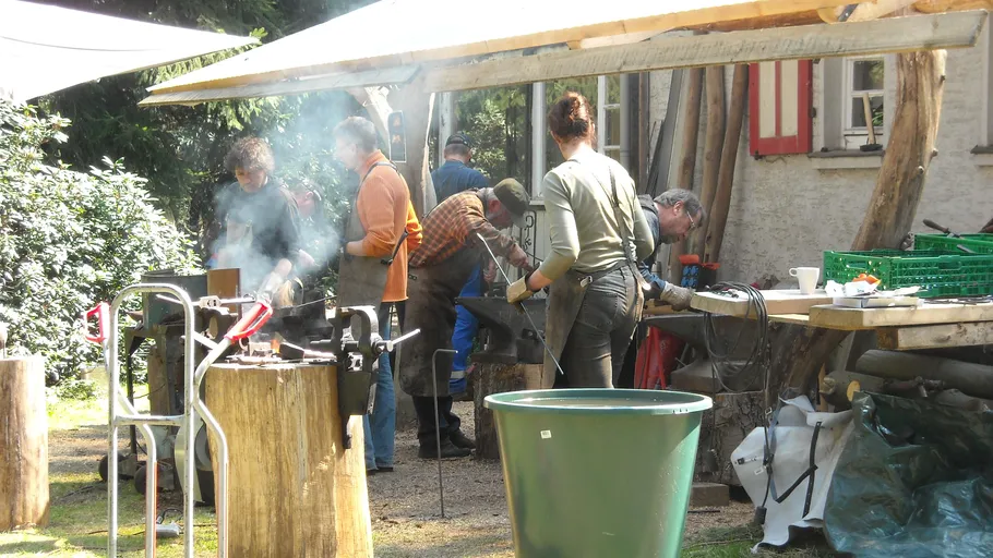 People blacksmithing outdoors under a canopy.