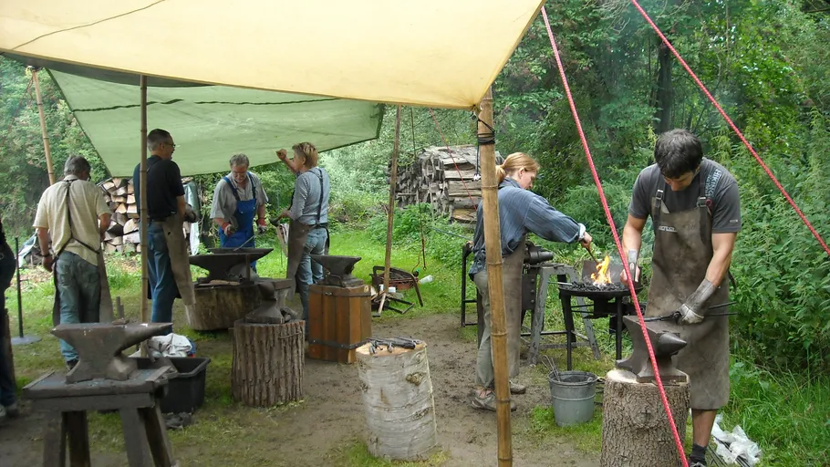Blacksmith workshop outdoors with participants forging metal.