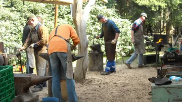 Menschen, die draußen in der Nähe von Ambossen und Bäumen schmieden.