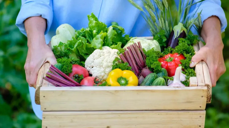 Person holding wooden box of fresh vegetables.