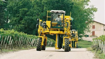 Weinbauerntemaschine fährt auf dem Weg, Bäume umgeben.