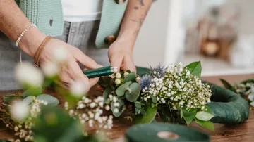 Person, die einen Blumenkranz auf dem Tisch zusammenbaut.