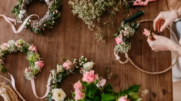 Person, die Blumenkränze auf einem Holztisch bastelt.