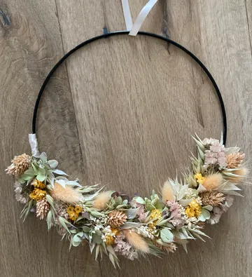 Blumiger Reifkranz mit getrockneten Blumen auf Holzoberfläche.