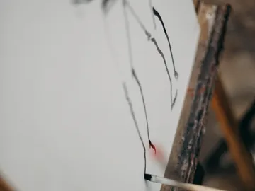 Ein Pinsel malt rote und schwarze Linien auf Leinwand.