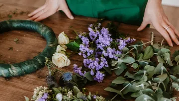 Hände arrangieren Blumen für einen Kranz auf dem Tisch.