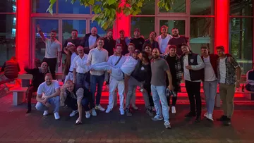 Group of people posing outside under red lights.