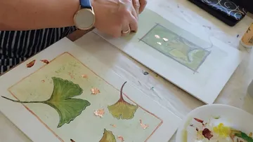 Person painting ginkgo leaves with gold leaf accents.