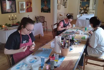 Three women painting at a table with art materials.