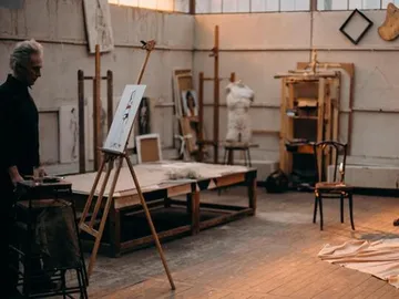 Ein Künstler steht vor einer Leinwand in einem Atelier.
