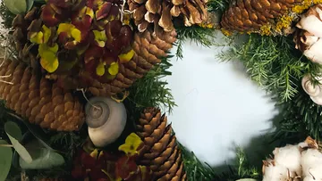 Dekorativer Kranz mit Tannenzapfen und Blumen.