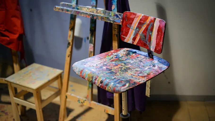 Mit Farbe bespritzter Stuhl und Staffelei im Studio.