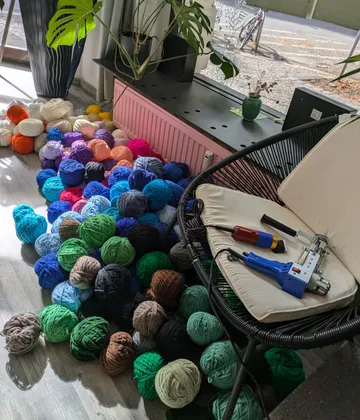 Balls of yarn scattered on the floor, near a chair with a tool on it, in a sunlit room.