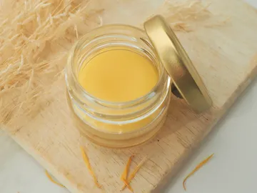 Ein Glas mit gelbem Balsam steht auf einem Holzbrett.