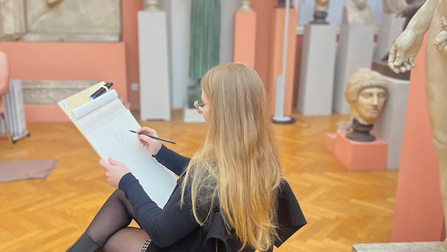 Person sketching in art gallery, surrounded by sculptures.