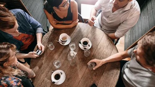 People seated around table with coffee cups.