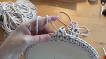 Ein Seil von Hand um einen Holzsockel häkeln.