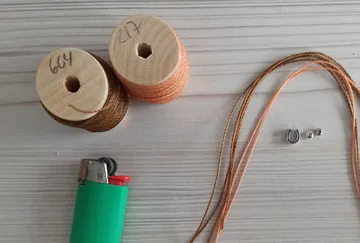 Fäden, Feuerzeug, Anhänger auf Holzoberfläche.