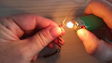 Hands using lighter to seal woven cord.