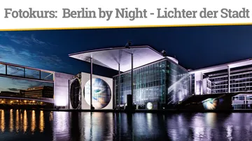 Modern buildings illuminated at night beside a river.