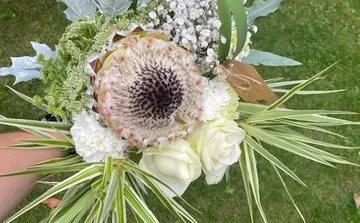 Bouquet with protea and roses outdoors.