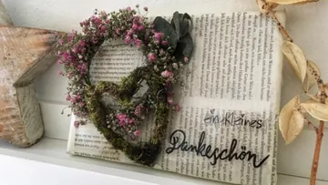 Herzförmiger Blumenkranz auf Zeitung mit Text.