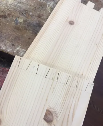 Holzbrett mit markierten Schwalbenschwanzschnitten auf der Werkbank.