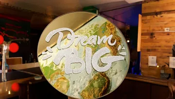 Rundes Schild mit dem Text „Dream Big“ im Café.